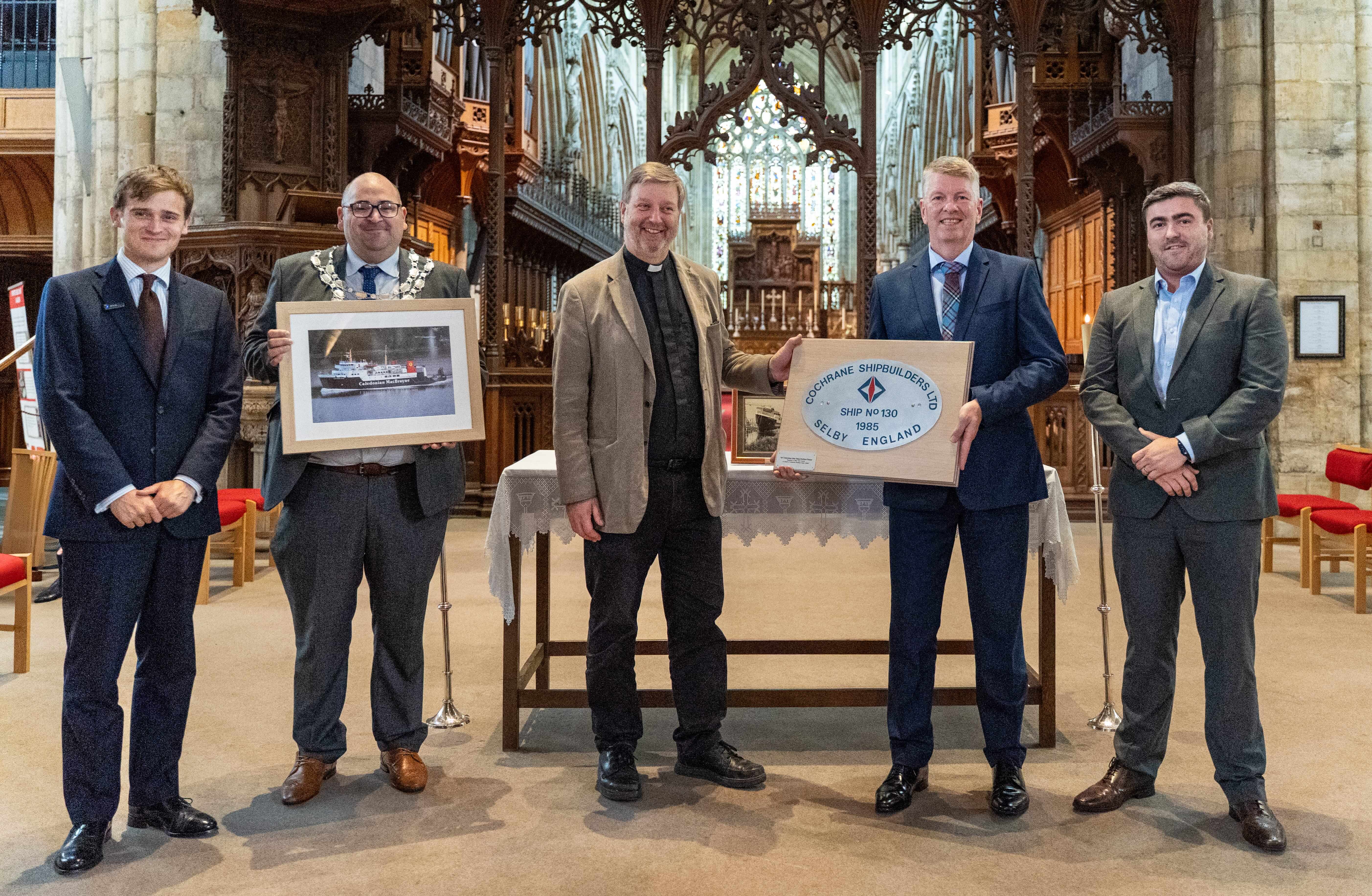 Photo of 5 people holding a plaque and photo